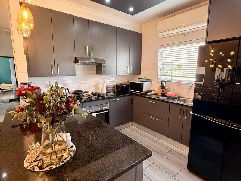 Modern kitchen featuring dark cabinetry, granite countertops, a central island, built-in appliances, and recessed ceiling lighting.