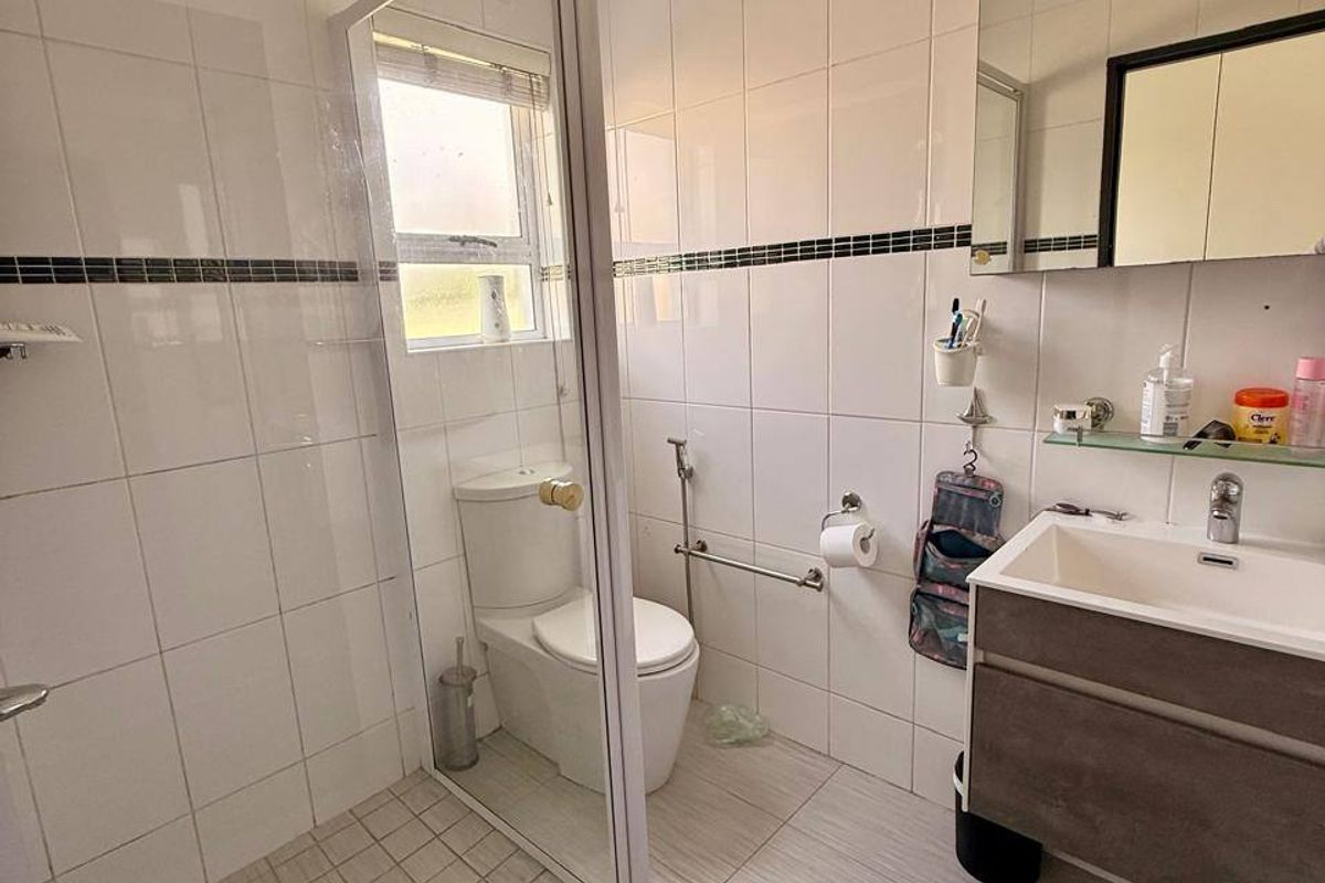 A functional bathroom featuring a glass-enclosed shower, a modern vanity cabinet, and neutral wall tiling throughout.