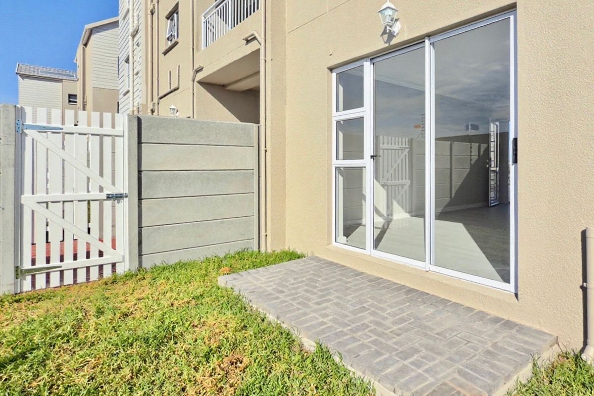 Rear view of the apartment featuring a paved patio area, sliding glass door access, and a private garden enclosed by a precast concrete wall.