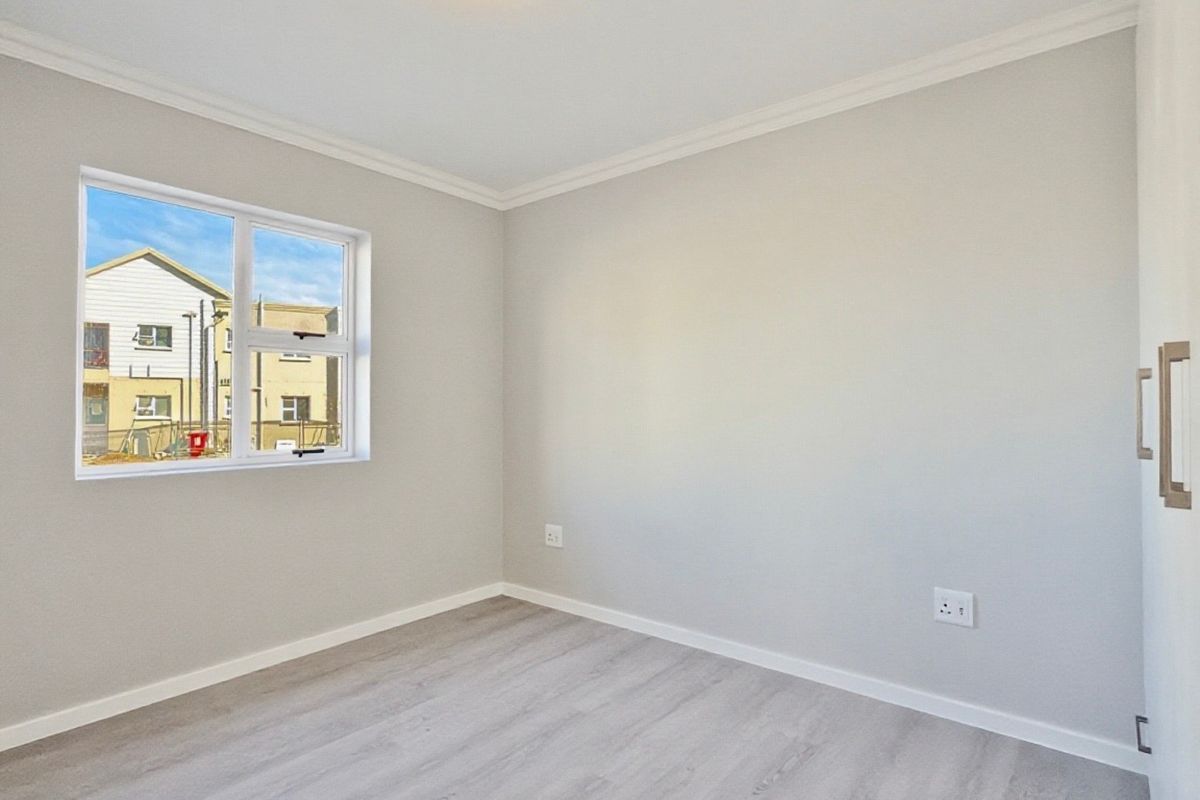 A bright, empty bedroom featuring modern light-toned laminate flooring, neutral walls, ceiling cornice, and a built-in cupboard.