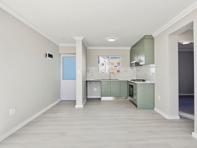 Modern open-plan kitchen featuring sage green cabinetry, marble-look splashbacks, integrated appliances, and light laminate flooring in a bright, neutral living space.