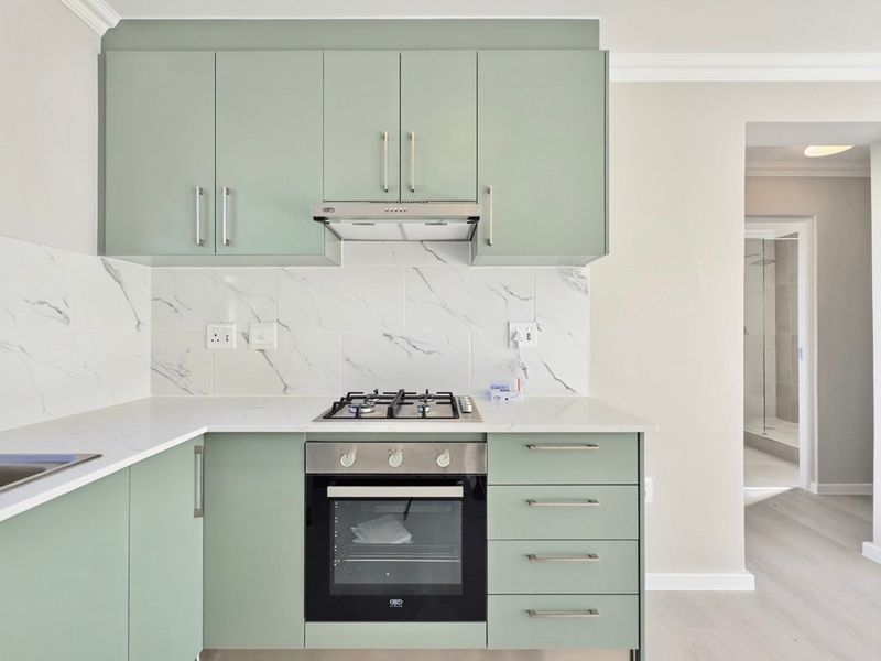 Modern kitchen featuring sage green cabinetry, stone countertops, marble-look splashback, and integrated stainless steel appliances including a gas hob and oven.