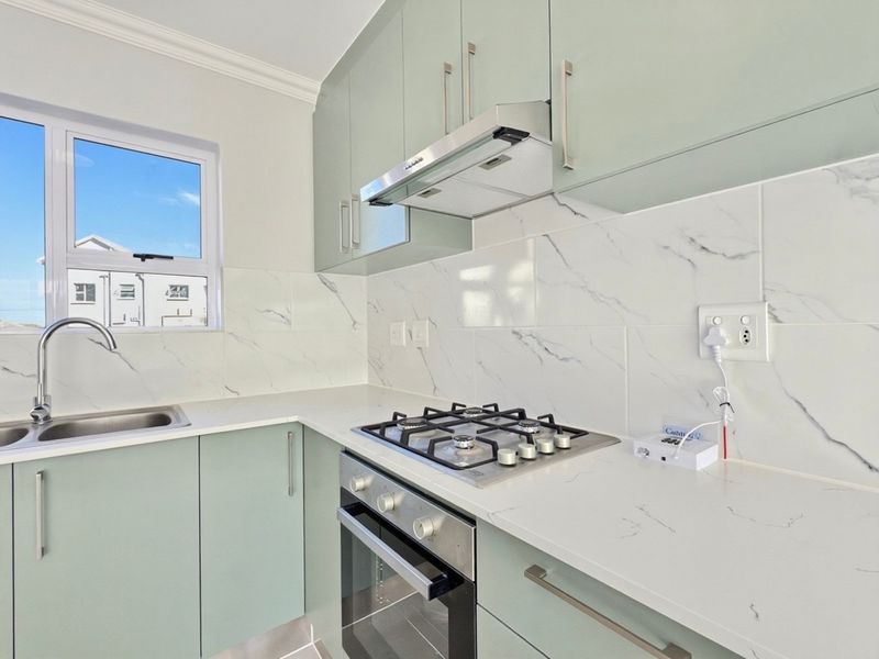 Modern kitchen featuring light green cabinetry, marble-look tiled backsplash, quartz countertops, and integrated stainless steel appliances including a gas hob and oven.