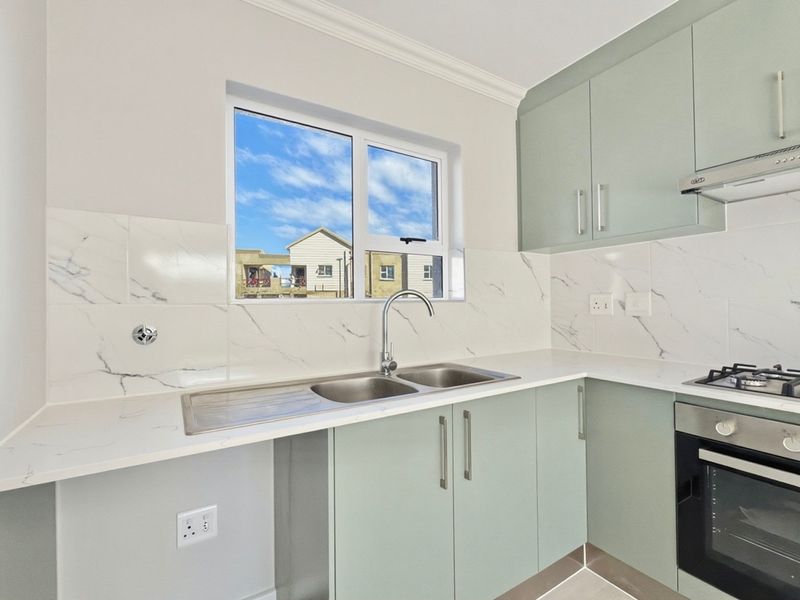 Modern kitchen featuring light green cabinetry, marble-look splashback, stone countertops, built-in oven, gas hob, and a double sink with a mixer tap.