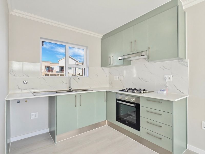 Modern kitchen featuring light green cabinetry, stone countertops, marble-look backsplash, and integrated stainless steel appliances including a gas hob and oven.