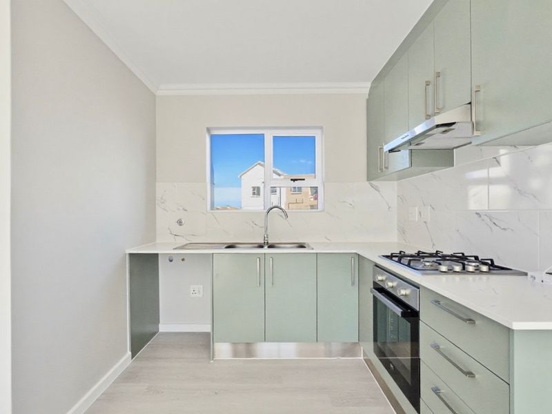 Modern kitchen featuring light green cabinetry, marble-look splashbacks, gas hob, built-in oven, and stainless steel sink with ample counter space.