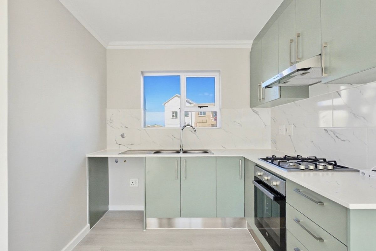 Modern kitchen featuring light green cabinetry, marble-look splashbacks, gas hob, built-in oven, and stainless steel sink with ample counter space.