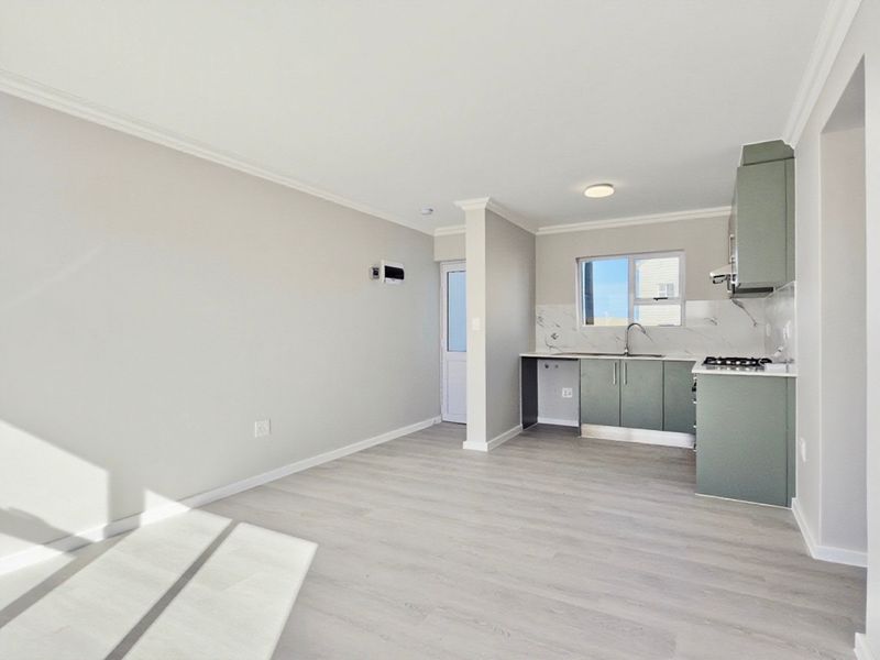 Modern open-plan living area featuring a sleek kitchen with sage green cabinetry, marble-look backsplash, gas hob, and light laminate flooring throughout.