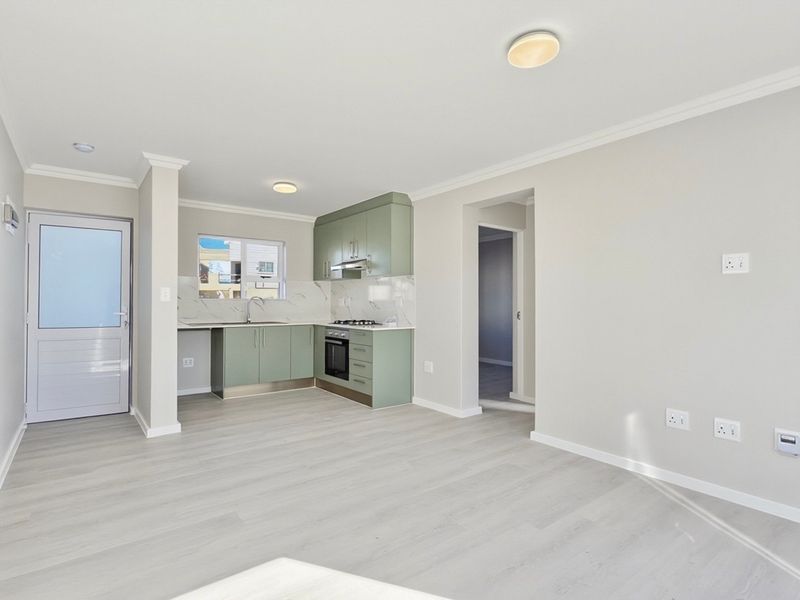 Modern open-plan kitchen and living area featuring light laminate flooring, sage green cabinetry, and integrated appliances in a clean, neutral space.