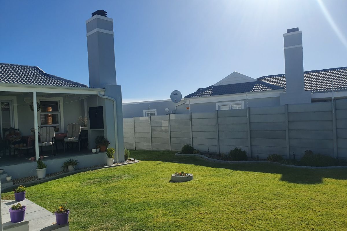 A well-maintained rear garden featuring a covered patio, built-in fireplace chimney, and secure precast concrete boundary walling.