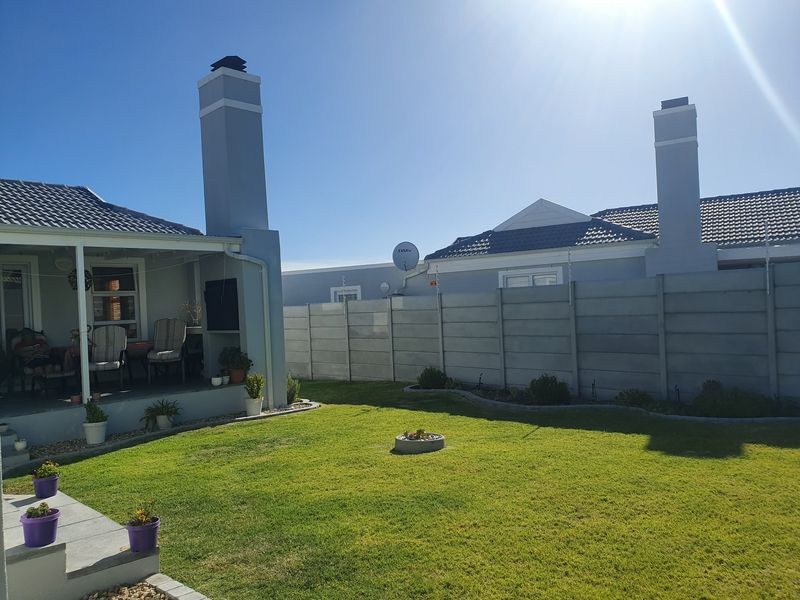 A well-maintained rear garden featuring a covered patio, built-in fireplace chimney, and secure precast concrete boundary walling.