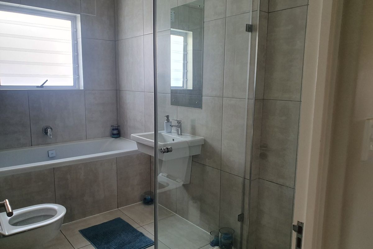 Modern bathroom featuring a built-in bathtub, wall-mounted basin, and a glass-enclosed shower with neutral floor-to-ceiling tiling.