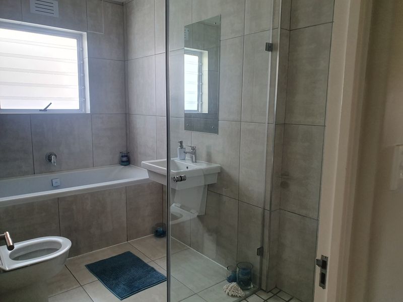 Modern bathroom featuring a built-in bathtub, wall-mounted basin, and a glass-enclosed shower with neutral floor-to-ceiling tiling.