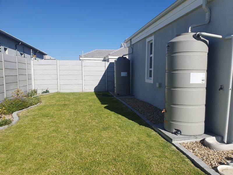 Rear garden area featuring a well-maintained lawn, precast concrete boundary wall, and two installed water storage tanks connected to the building's gutter system.