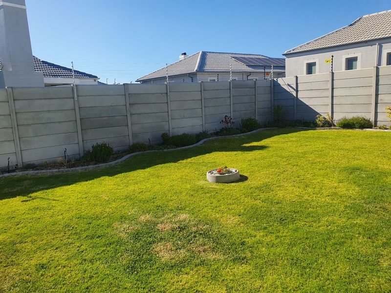 A well-maintained private garden featuring a manicured lawn, bordered by precast concrete walls equipped with electric fencing for added security.