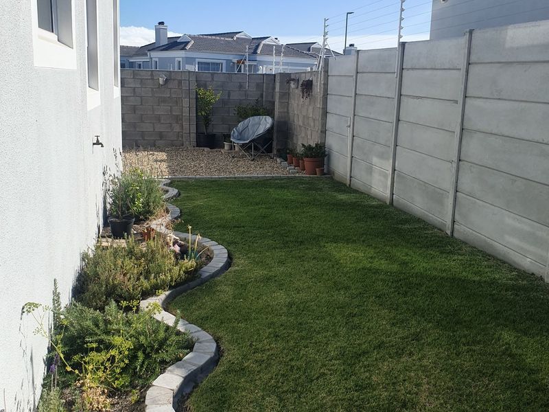A well-maintained rear garden featuring a manicured lawn, curved concrete-edged garden beds, gravel utility area, and secure perimeter walling with electric fencing.