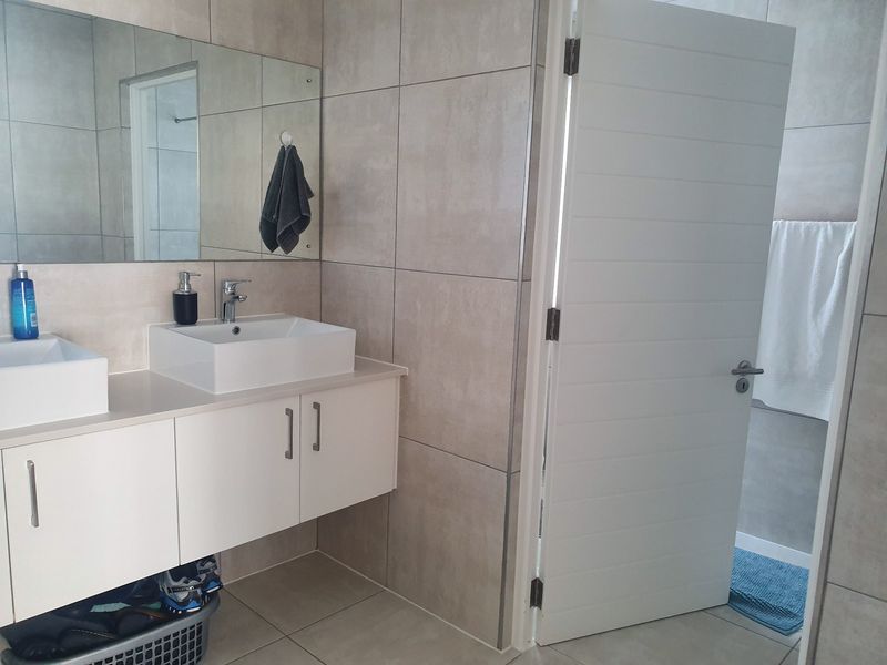 Modern bathroom featuring a double vanity with wall-mounted cabinetry, large mirror, and neutral floor-to-ceiling tiling.