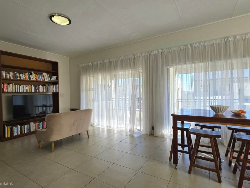 Spacious open-plan living and dining area featuring neutral tiled flooring, a large built-in shelving unit, and expansive sliding glass doors leading to a balcony.