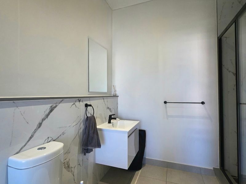 Modern bathroom featuring a wall-mounted vanity, marble-look wall tiling, a toilet, and a glass-enclosed shower with contemporary black fixtures.