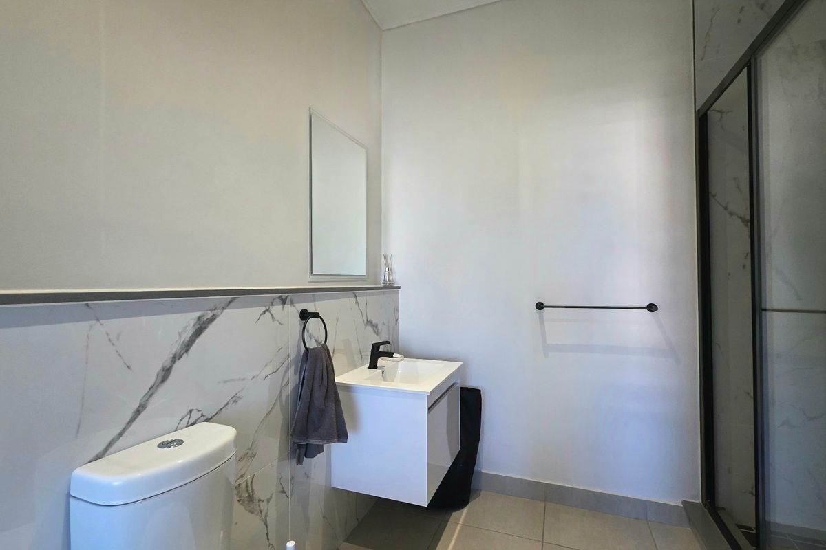 Modern bathroom featuring a wall-mounted vanity, marble-look wall tiling, a toilet, and a glass-enclosed shower with contemporary black fixtures.