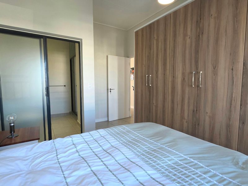 A well-maintained bedroom featuring extensive built-in wooden cupboards, tiled flooring, and a modern sliding glass door leading to an adjacent space.