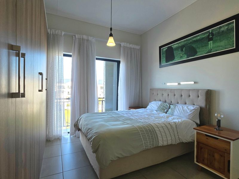 A well-maintained bedroom featuring built-in wardrobes, tiled flooring, and a sliding glass door providing access to a balcony.