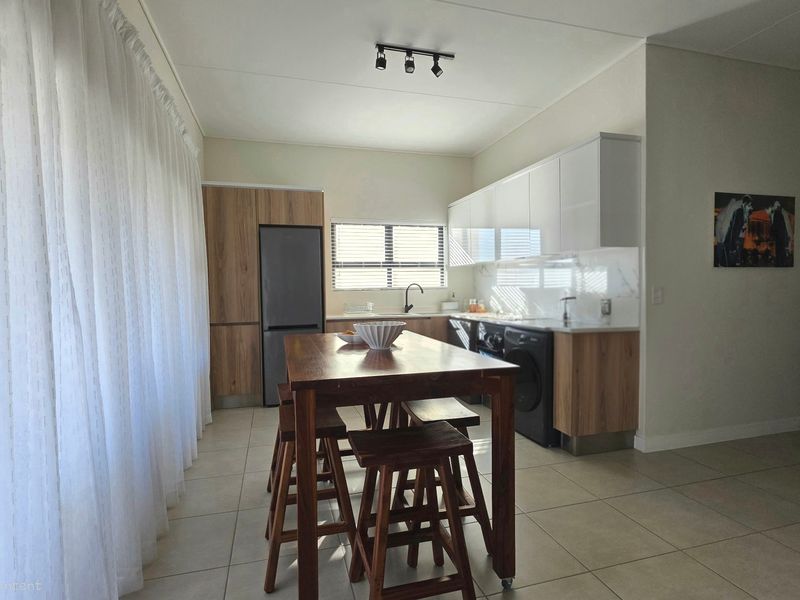 Modern open-plan kitchen featuring sleek two-tone cabinetry, marble-look backsplash, and tiled flooring, seamlessly integrated with the living area.