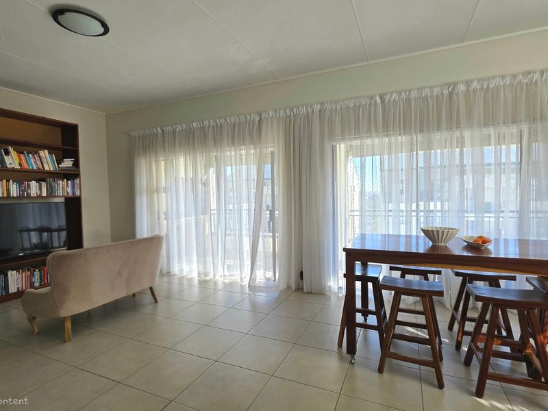 Spacious open-plan living and dining area featuring tiled flooring, built-in shelving, and large sliding glass doors leading to an outdoor space.