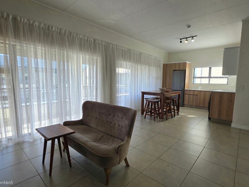 Open-plan living and kitchen area featuring tiled floors, modern wood-finish cabinetry, and large sliding glass doors providing ample natural light.