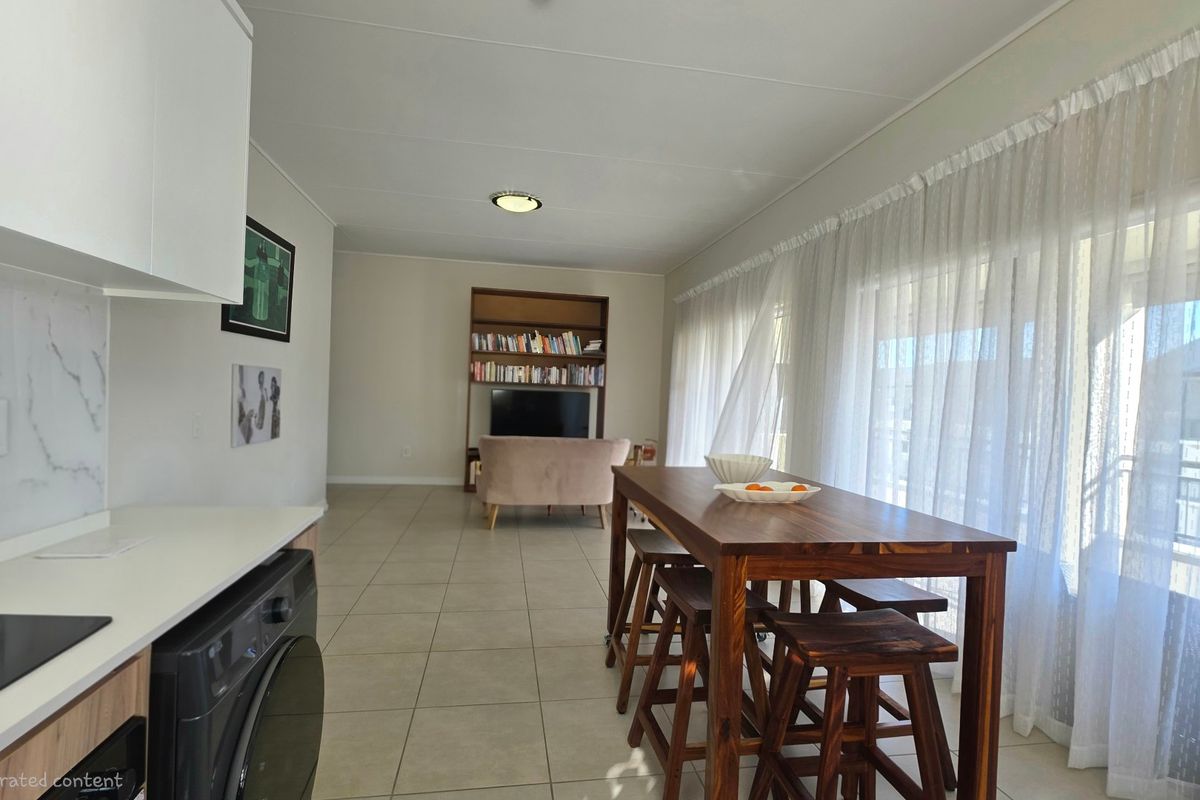 Open-plan living and kitchen area featuring tiled floors, modern cabinetry, marble-look splashback, and large sliding doors leading to an outdoor space.