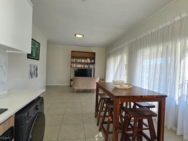 Open-plan living and kitchen area featuring tiled floors, modern cabinetry, marble-look splashback, and large sliding doors leading to an outdoor space.