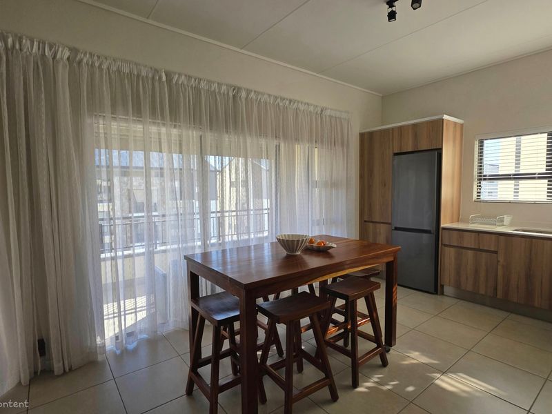 Open-plan kitchen and dining area featuring modern wood-finish cabinetry, tiled flooring, and a large sliding door providing access to the balcony.