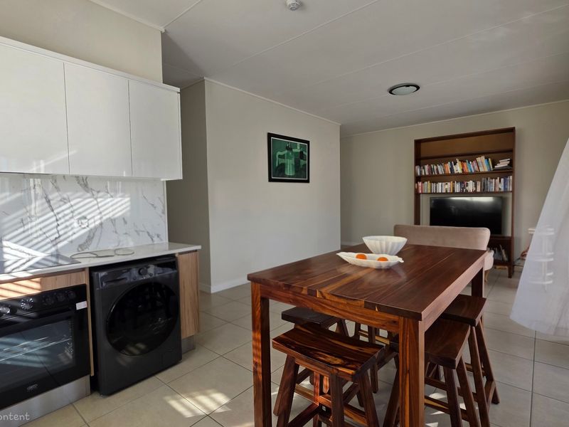 An open-plan living and kitchen area featuring modern cabinetry, a marble-look splashback, built-in oven, and tiled flooring throughout.