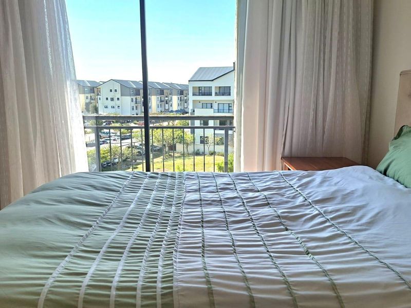 A bright bedroom featuring a built-in wardrobe and a sliding glass door that opens onto a balcony with neighborhood views.