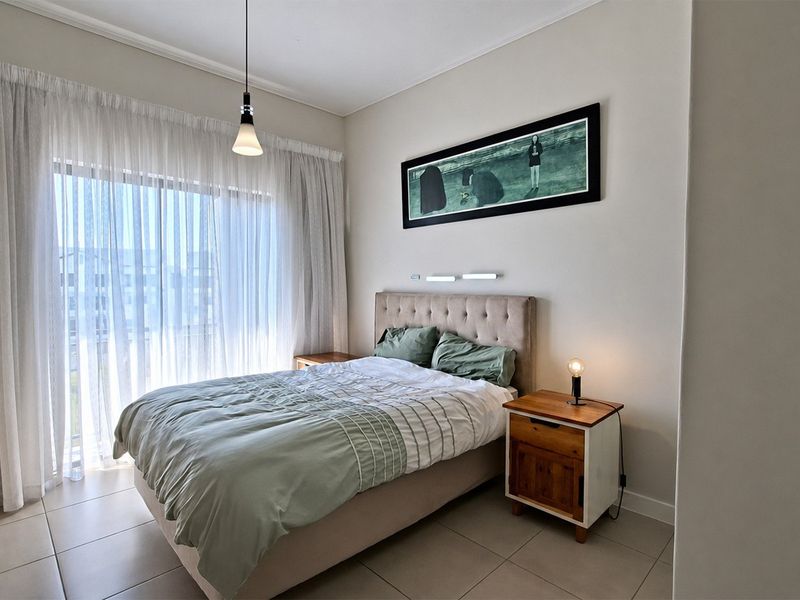 A well-maintained bedroom featuring tiled flooring, a built-in wardrobe, and a large sliding glass door providing natural light.