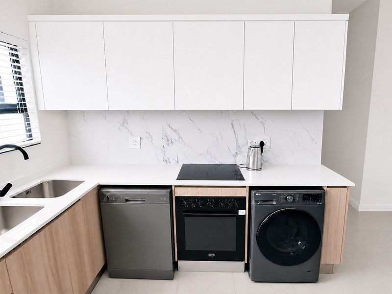 Modern kitchen featuring sleek white cabinetry, marble-look splashback, integrated electric hob, built-in oven, and double undermount sink with contemporary black fixtures.
