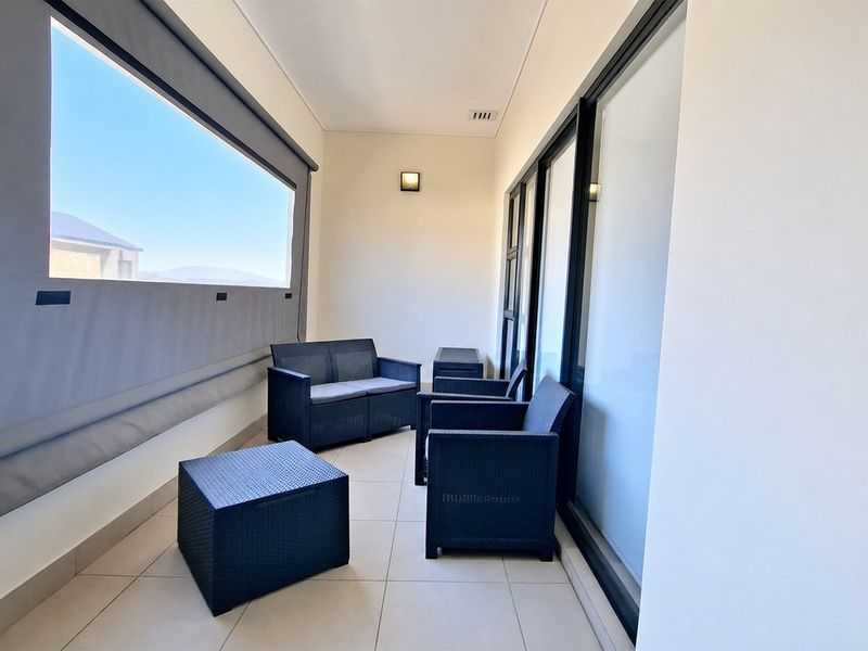 A covered balcony featuring tiled flooring, sliding glass doors, and a retractable outdoor blind, providing a functional and well-maintained outdoor living space.