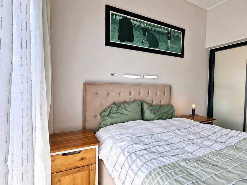 A well-maintained bedroom featuring neutral tones, wall-mounted reading lights, and a sliding door providing access to an en-suite bathroom.
