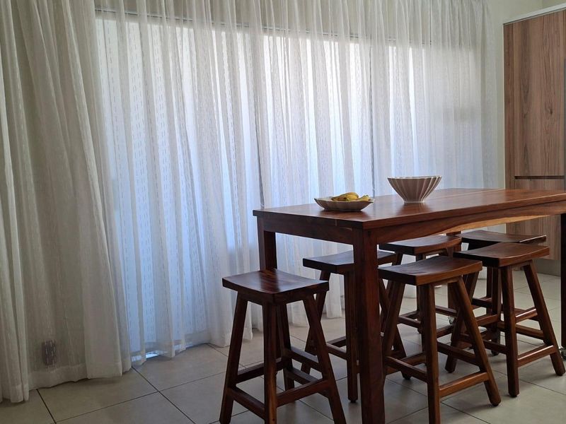 An open-plan living and kitchen area featuring tiled flooring, modern built-in cabinetry, and large sliding glass doors with sheer curtains for natural light.