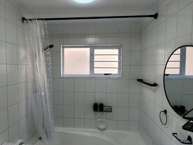 A functional bathroom featuring white wall tiles, a bathtub with a shower curtain, and a frosted glass window for privacy.