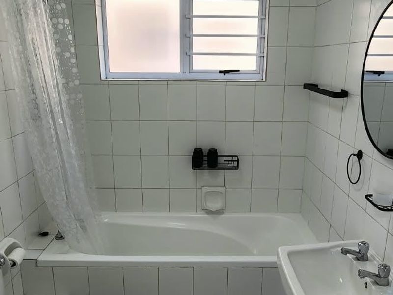 A functional bathroom featuring a bathtub with shower attachment, wall-mounted basin, and toilet, finished with white wall and floor tiles.