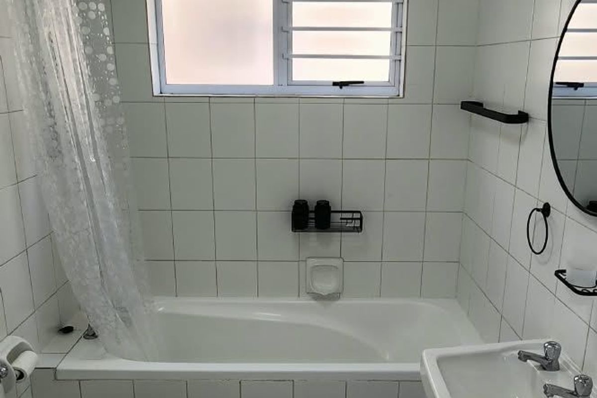 A functional bathroom featuring a bathtub with shower attachment, wall-mounted basin, and toilet, finished with white wall and floor tiles.