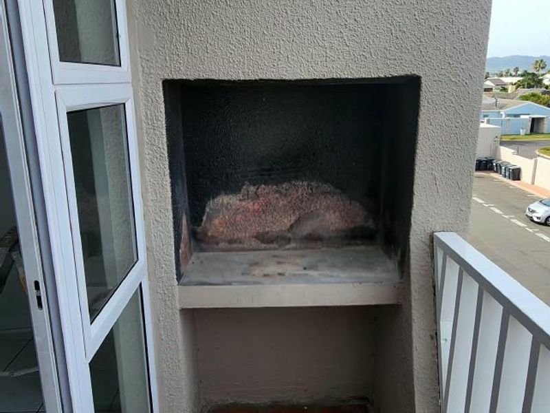 A balcony featuring a built-in braai, tiled flooring, and a metal balustrade, offering an outdoor space for grilling and relaxation.