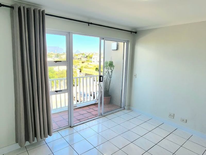 A bright, empty bedroom featuring tiled flooring and a sliding glass door that opens onto a private balcony.