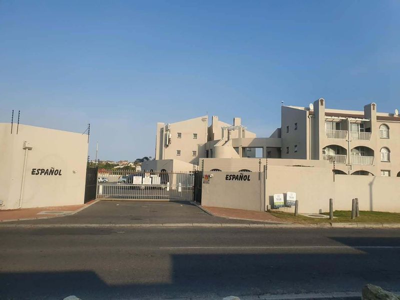 Front exterior view of the Español apartment complex, featuring secure gated access, perimeter wall with electric fencing, and multi-story residential units with balconies.