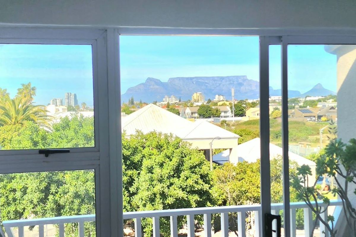 A scenic view of Table Mountain and the surrounding urban landscape captured through a sliding glass door and balcony railing.