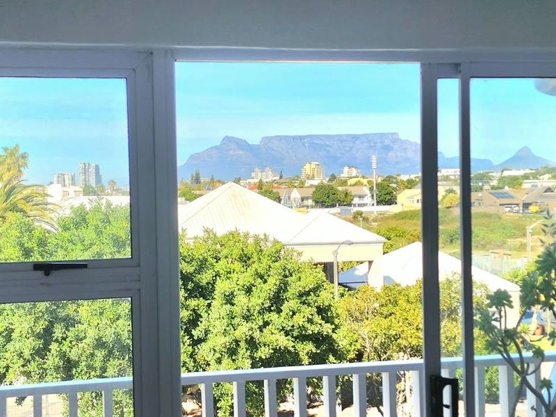 A scenic view of Table Mountain and the surrounding urban landscape captured through a sliding glass door and balcony railing.