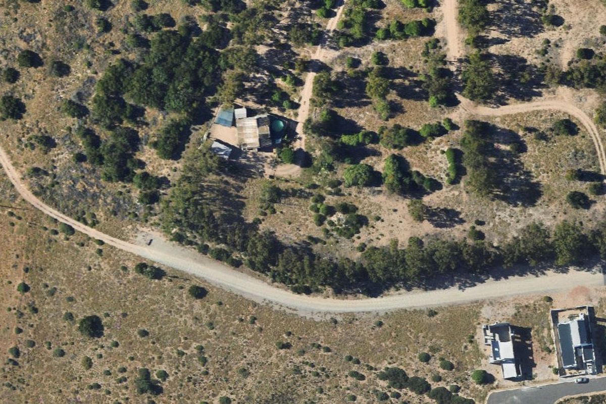 Aerial view of a vacant residential plot featuring natural vegetation, existing structures, and access via an unpaved road.