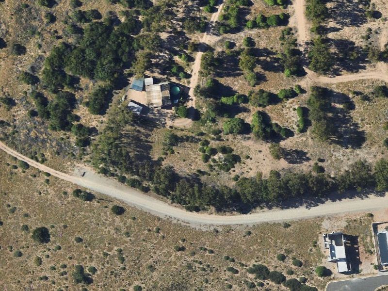 Aerial view of a vacant residential plot featuring natural vegetation, existing structures, and access via an unpaved road.