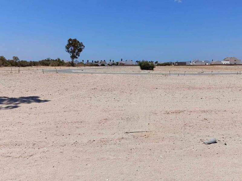 A vacant residential plot featuring a level surface, boundary markers, and access to a paved road in a developing neighborhood.